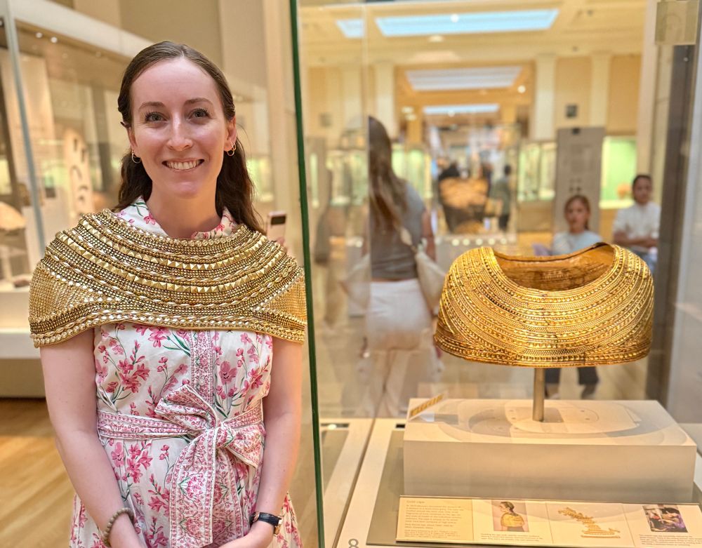 Woman wearing a beaded version of the golden Mold Cape from Wales, an impressive early Bronze Age creation. The woman is standing beside the original wearing her creation.