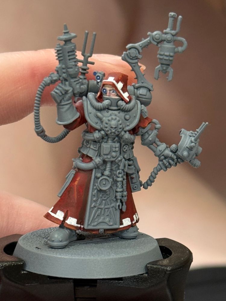 A tech priest miniature arrayed in lots of cybernetic gear, half-painted 