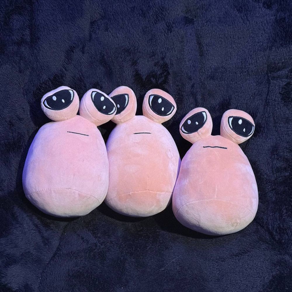Three pou plushies on a dark background facing the camera.