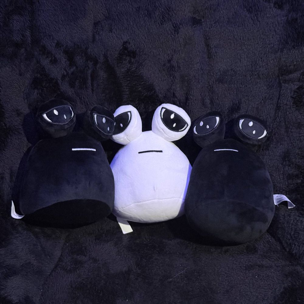 Three pou plushies on a dark background facing the camera.
The pou colors are in order: black, white, black.