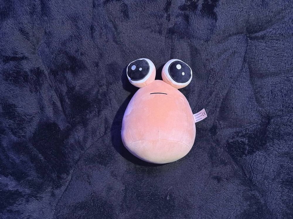 Pou behind the same dark background, but this pou has different eyes.
They're fully circular instead of being a semi-circle.
Looks a little bit like the eyes on a pleading face emoji.