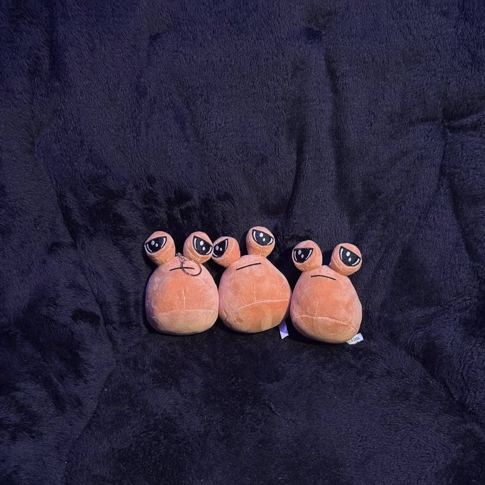 Three small pous behind a dark background. They're keychains with a chain and a ring attached to the top of the pou.