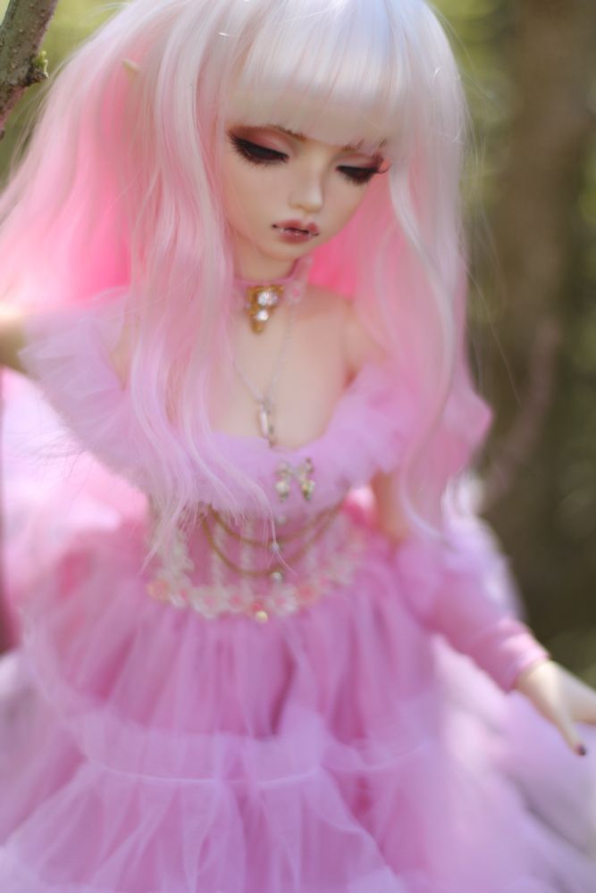 A pink haired doll in a pink frilly dress with vampire teeth. 
