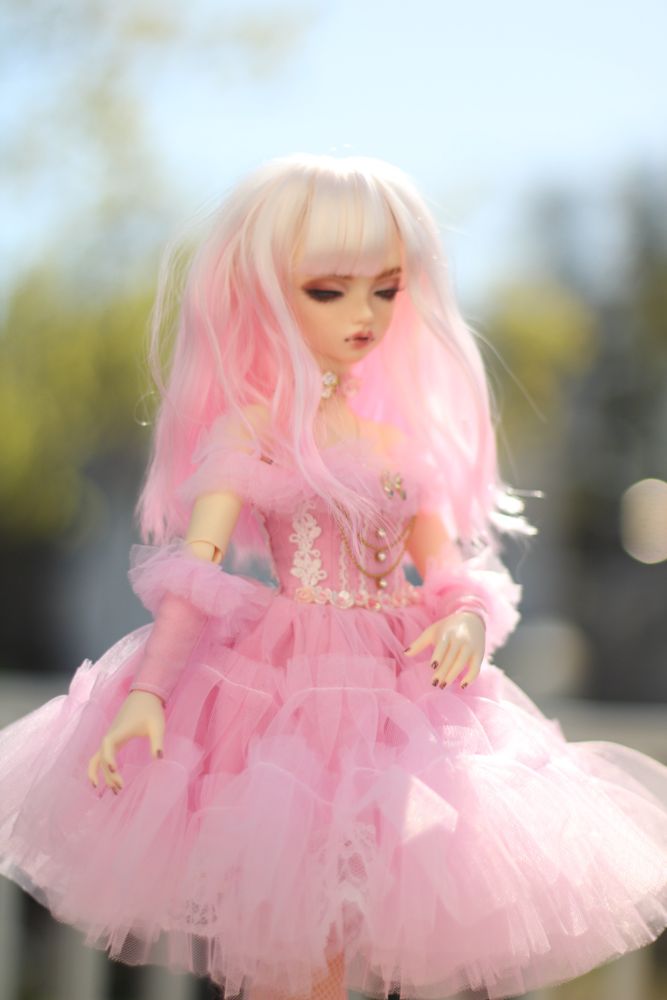 A pink haired doll in a pink frilly dress with vampire teeth. 