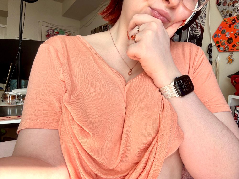 photo of Lanie’s upper torso, she’s wearing a loose peach colored tee and making a thinking face hand gesture 