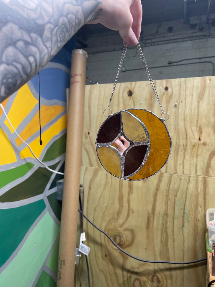 stained glass moon that is yellow connected to dark brown and tan with a small mirror of a star in the middle 