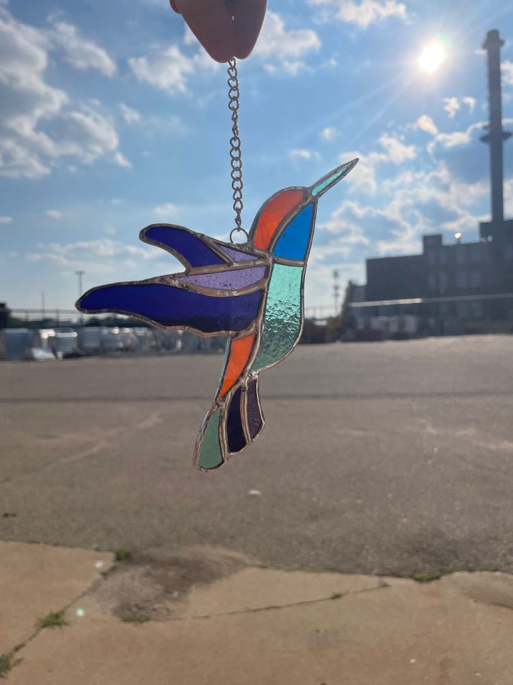 stained glass of a hummingbird made out of the colors: blue, dark purple, light purple, and orange