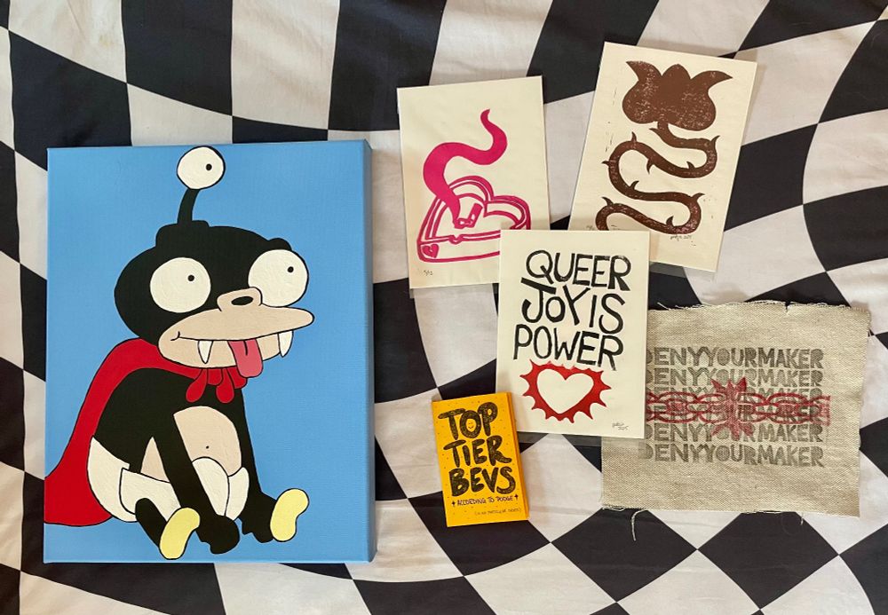 photo of a prize pool that can be won, it includes: a 11x17 acrylic painting of Nibbler from Futurama on a light blue background. A small yellow zine that says “top tier bevs” filled with drawings of Podge’s favorite drinks. A print of a rose with a curve stem and thorns made of black ink on white paper. A heart shaped ash tray with smoke coming from it in pink on white paper. A print that says “queer joy is power” in black ink with a jagged pointy heart in red ink underneath on white paper. A canvas patch with the words “deny your maker” in black ink stacked 5 times on top of eachother with a red inked chain on top in the middle. All items on top of a wavy black and white checkered background. 