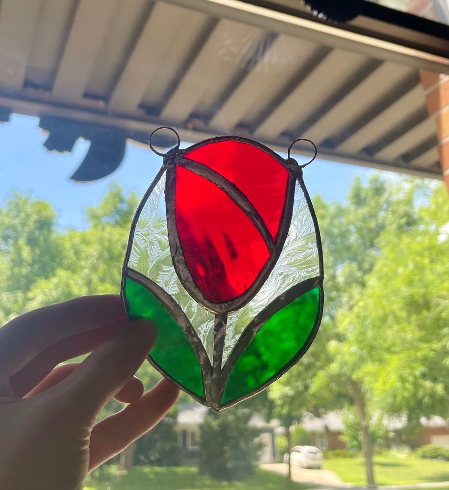 stained glass tulip that is red with green flowers with a clear glass in between/surrounding the leaves