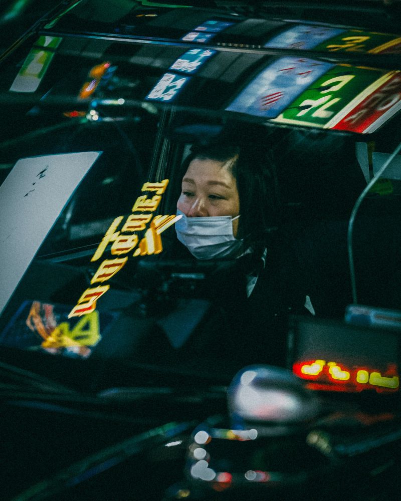 Photo of female taxi driver through the window with neon lights in the reflection 