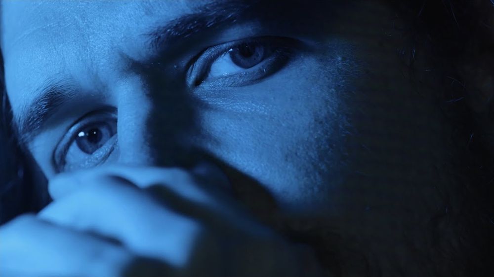 Thumbnail of Bo Burnham's "All Eyes on Me" Youtube video.  Close-up on Bo's face (thirty-year-old Caucasian male) tinted by blue light.  His mouth is angled toward the lower-left corner of the image, but it is covered by his out-of-focus hand.  His eyes are focused on the viewer.