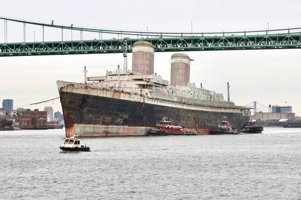 ocean liner SS United States being tugged out of the Philadelphia harbor, on her way to her final resting place off Destin-Fort Walton beach. her hull, once a gleaming black, is now very rusty. her once red funnels are so rusted that they're light pink now