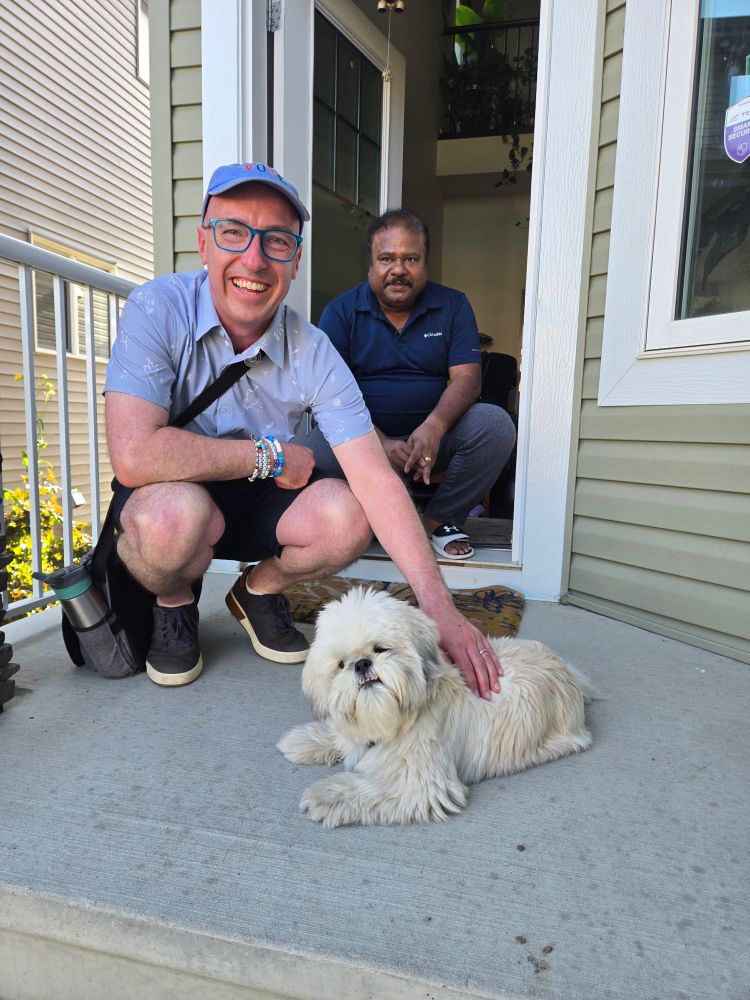 Andrew crouched down petting a dog with another person crouched down looking at the camera.