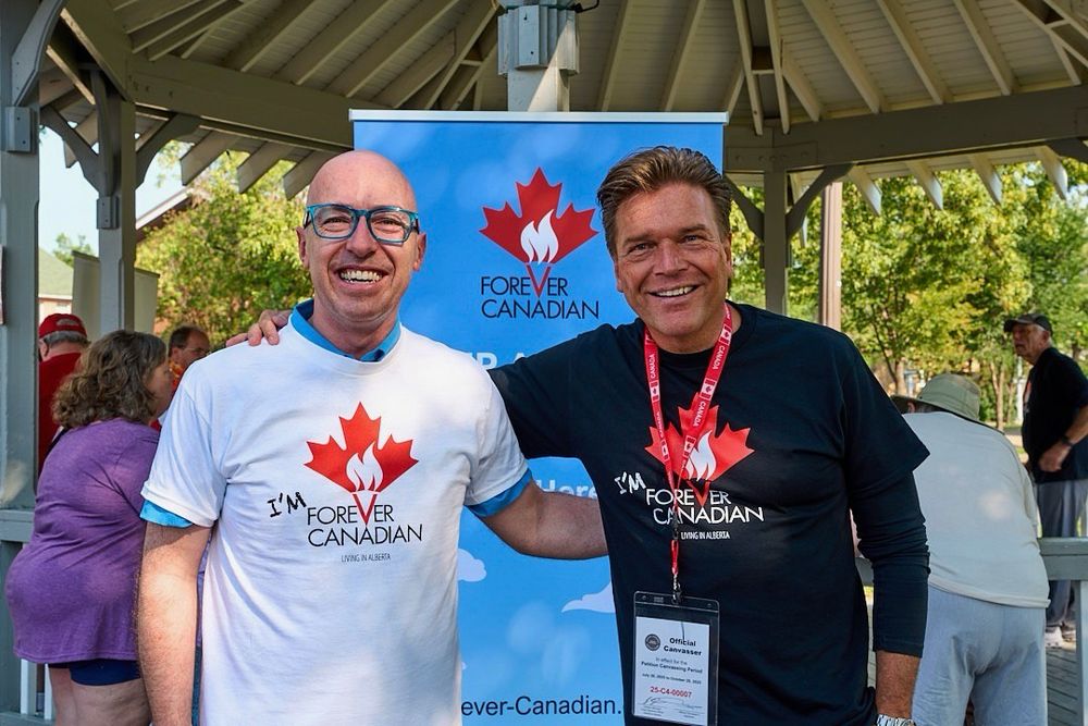 Andrew in a white shirt that says Forever Canadian and Thomas is a black Forever Canadian shirt standing in front of a blue banner that says Forever Canadian.