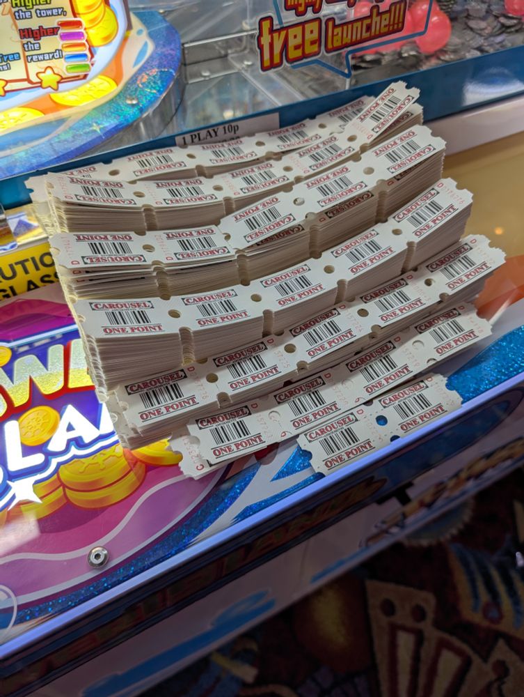 A photo of various paper tickets lined in piles on an arcade machine. Each ticket reads "CAROUSEL ONE POINT".