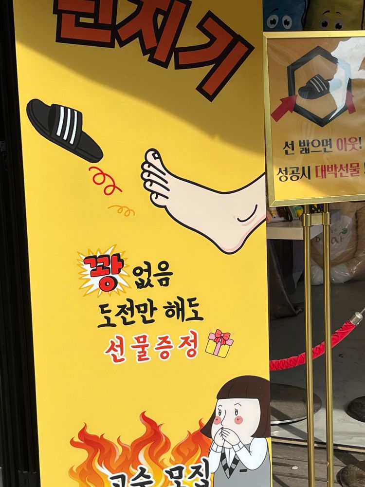 Sign is in Korean, which I don’t speak, but there is a picture of a foot kicking off a slipper and a cartoon character looking on in awe, as well as a picture of a present/prize