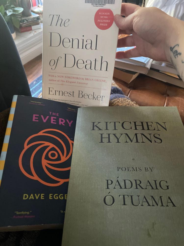 Three softcover books: “The denial of death”, “the every”, and “kitchen hymns”. 
