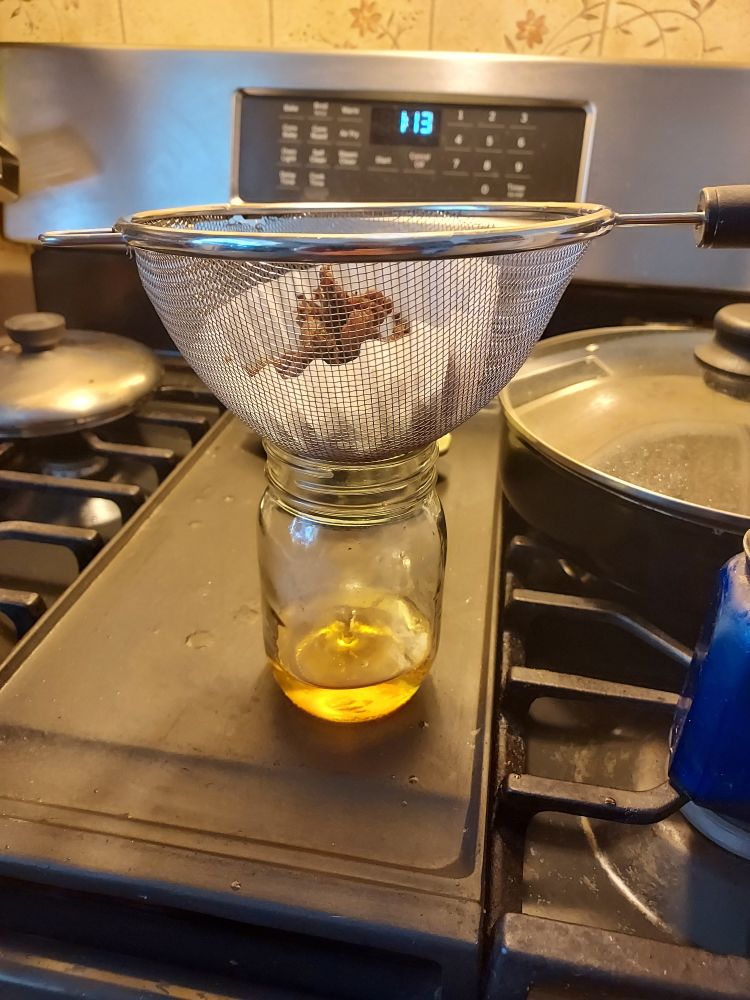 A bell jar about 1/4 full of yellow liquid. On top of it is a metal strainer containing a coffee filter and fried bits