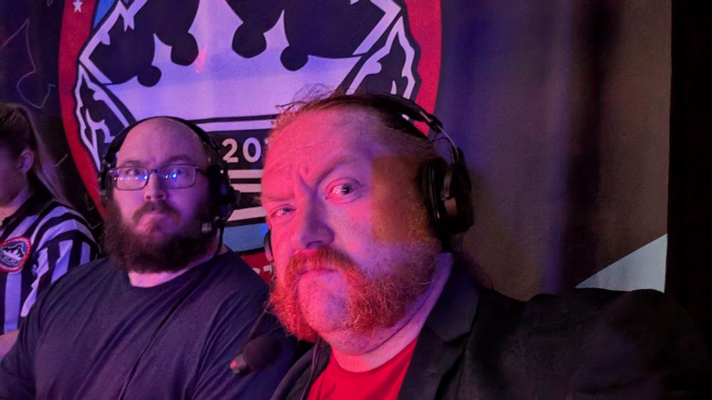 Two fine looking bearded gentlemen in headsets in front of a banner for a Newcastle Pro Wrestling show. Specifically The Buccaneer and Cam the Commentator.