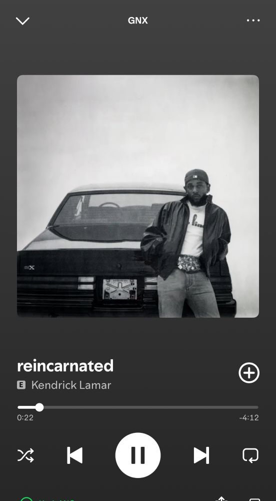 Screen grab from Spotify of “reincarnated” by Kendrick Lamar. The cover is a black and white photo of Kendrick leaning on the hood of a GNX muscle car. He’s wearing a white TV shirt, blue jeans, a black bomber (?), a baseball cap turned back and the biggest most baller belt you ever saw.