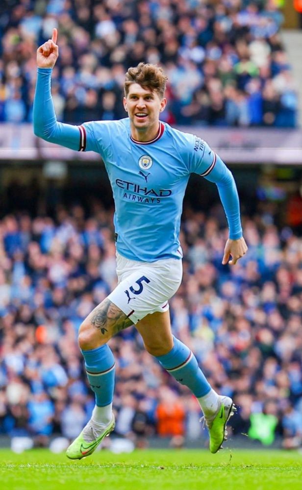 John Stones of Manchester City in a blue top and white shorts raising his hand in a number one