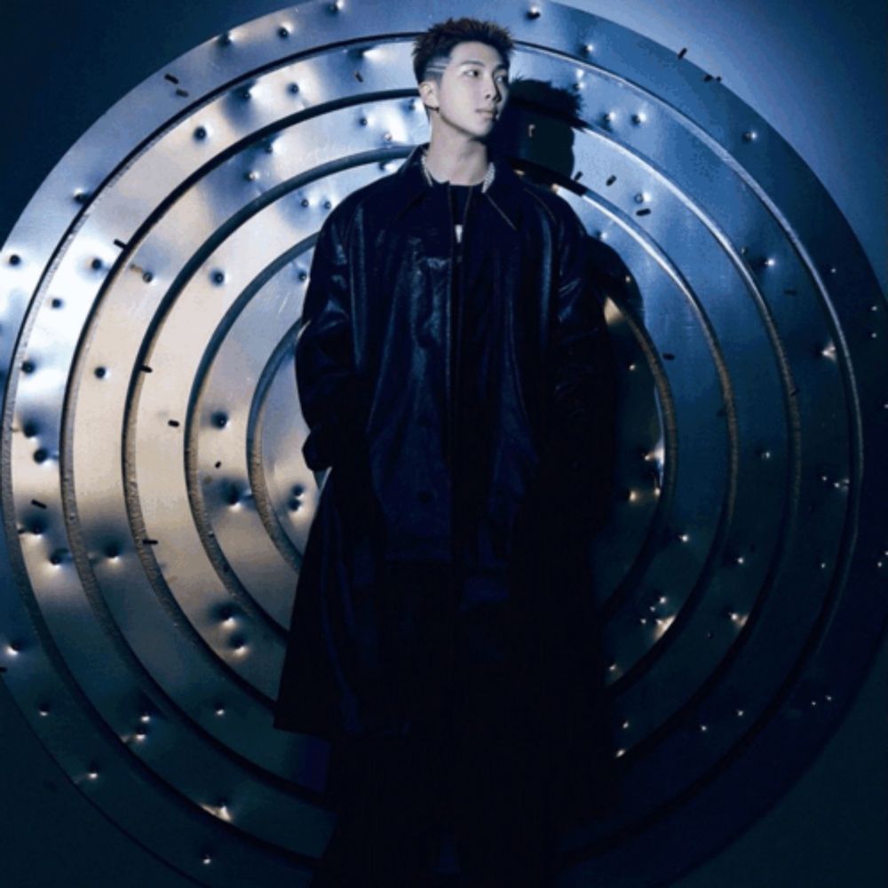 a man in a black coat stands in front of a circular metal wall