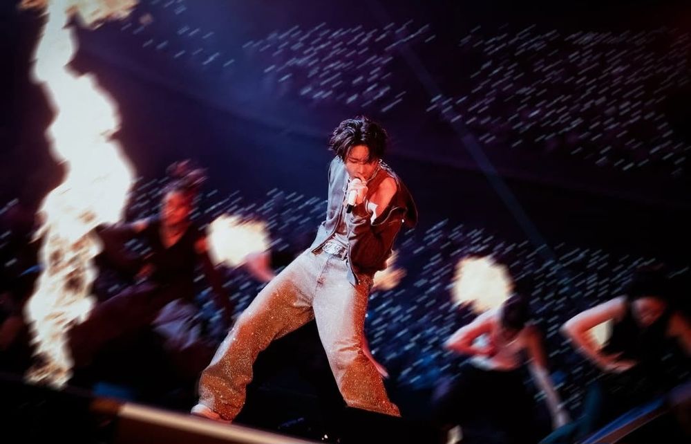 Hobi oerforming on stage sorrounded by dancers and flames.