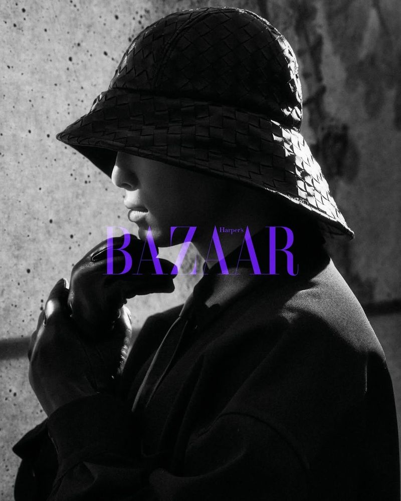 A black-and-white portrait of a model wearing a woven leather bucket hat, leather gloves, and dark clothing.

The model is positioned in profile.