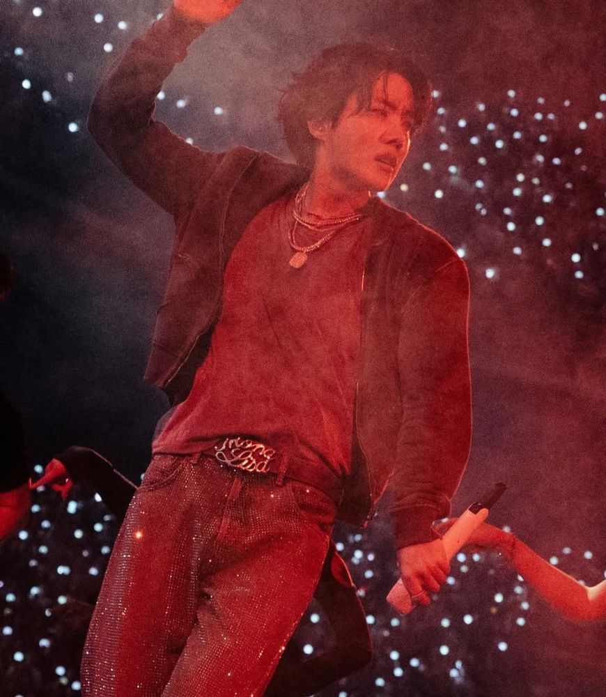 Close up photo of Hobi under a red light. Behind him you can see part of the crowd holding ARMY bombs.