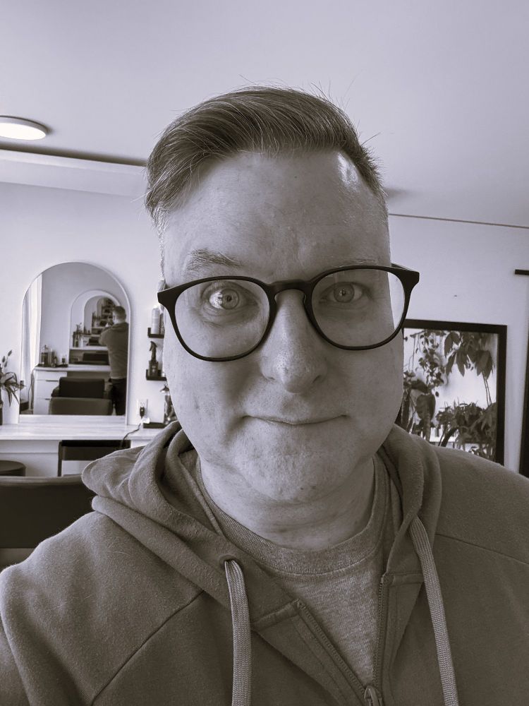 Black and white photo of a person in a hoodie and T-shirt. One eyebrow is making a power grab for full control of the face. 