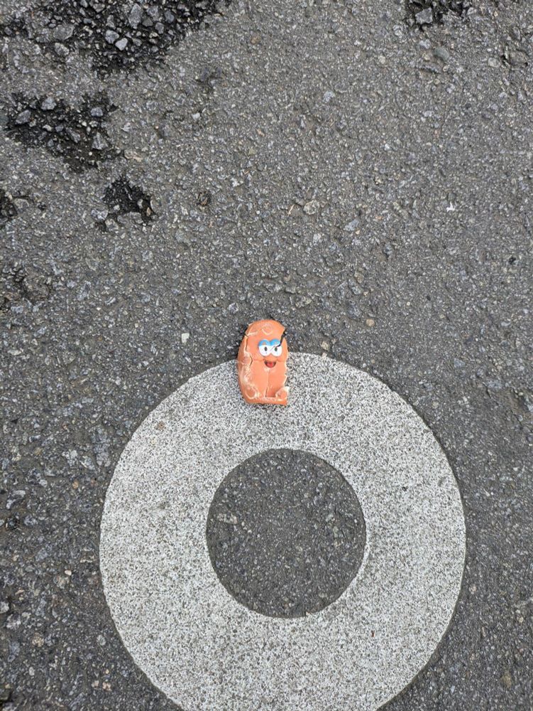 a broken and destroyed McDonald's chicken nugget toy, sitting on top of a large circle painted on the bitumen. his gaze is weary, literally cracked through into his eyes, as he stares skyward in silent contemplation of his misery. will the end come? or will his presence persist so long as his micro plastics remain ground into the pavement or washed into Vancouver's Coal Harbour, to rest on some unknown and foreign shore?