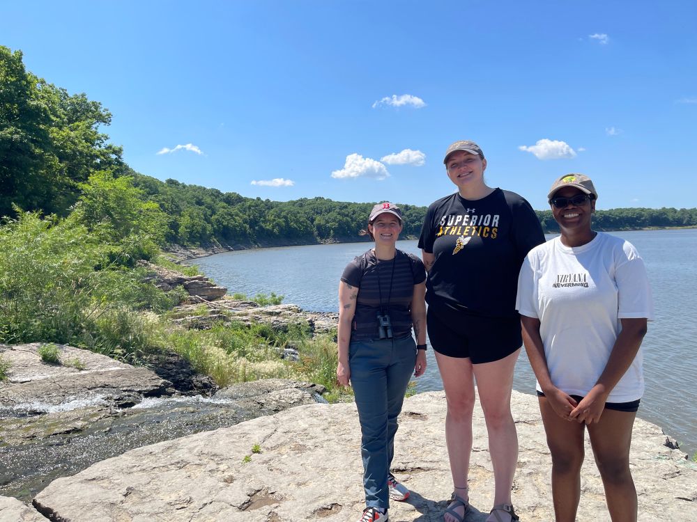 Three women standing on a rock overlooking a river