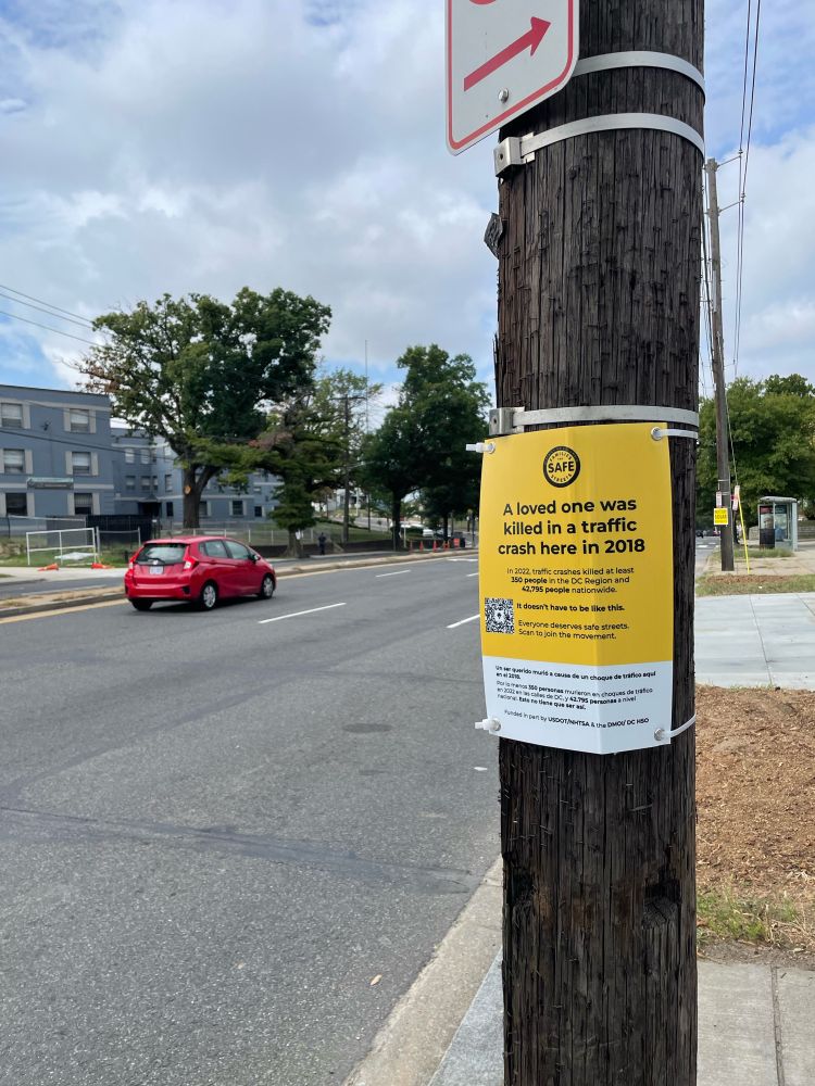 A yellow crash memorial sign next to a big street. 