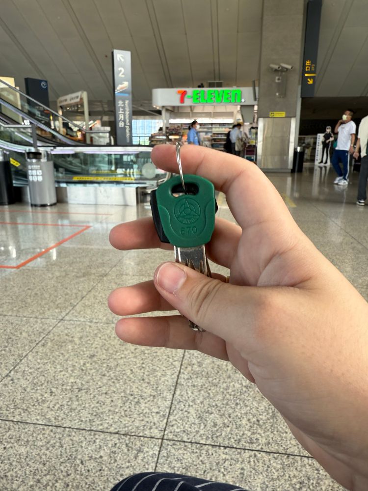 Apartment keys in the foreground. Photo was taken in a large high speed rail station in Hsinchu, Taiwan. There is a small 7-Eleven stand in the background. 
