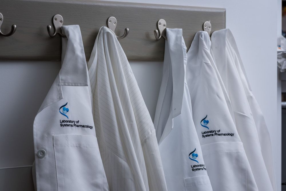 Lab coats branded with the Lab of Systems pharmacology hung up on hooks.
