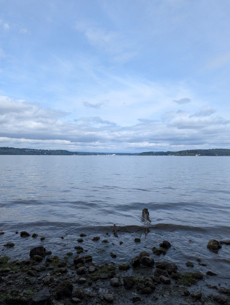 A view of the Puget sound past a rocky shoreline with a hazy mix of blue sky and clouds