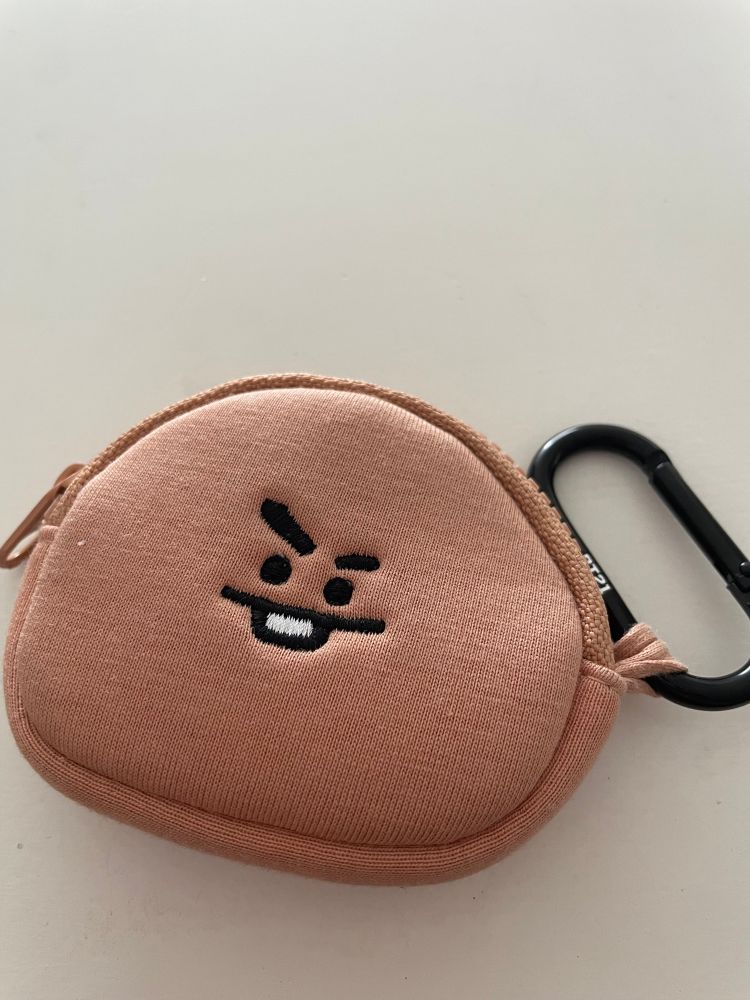 a tiny cocoa colored coin purse shaped like BT21 Shooky with his little mischievous face on it, clipped to a black carabiner 