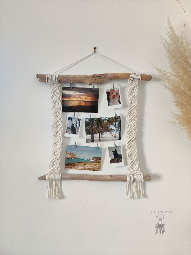 Le porte photo est accroché au mur. Il est constitué de 2 morceaux de bois flotté horizontaux rejoint entre eux par du macramé tissé en forme d'arabesque. 3 cordes sont accrochées au macramé de manière horizontale et des photos y sont épinglées grâce à des petites épingles.