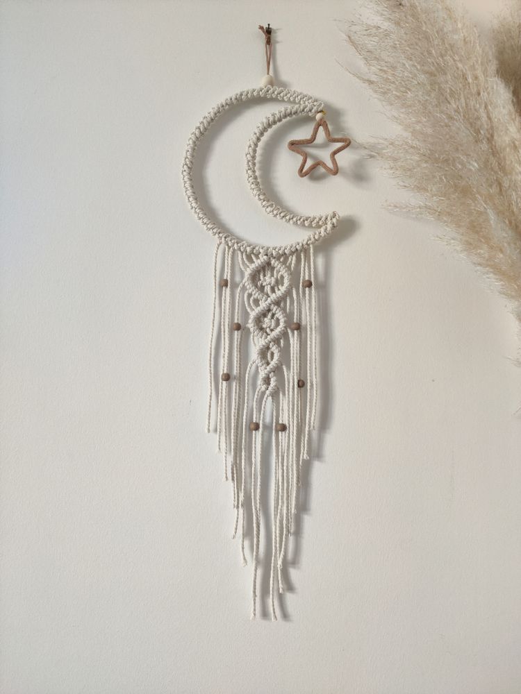 Lune en macramé blanc, dans le croissant de lune, une petite étoile marron. Une traîne en macramé est sous la lune, des petites perles marrons sont sur la traîne.
