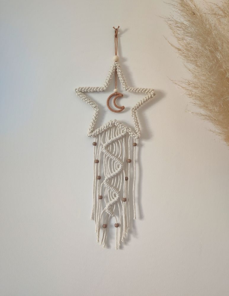 Etoile en macramé blanc, dans l'étoile une petite lune marron. Une traîne en macramé est sous l'étoile comme si c'était une étoile filante, des petites perles marrons sont sur la traîne.
