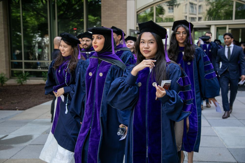 Graduates in purple academic regalia walk together outdoors on the Georgetown Law campus.
