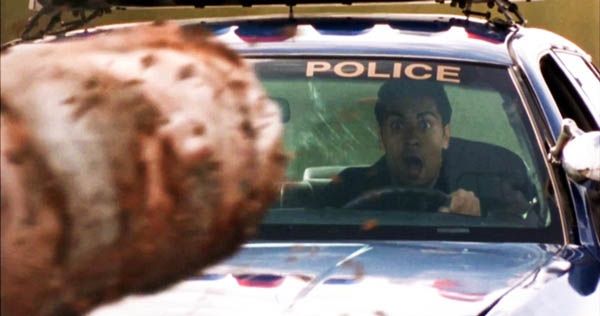 A still from the film Final Destination, showing the moment a huge log falls from a truck and ploughs through the windscreen of a police car, obliterating the officer behind the wheel.