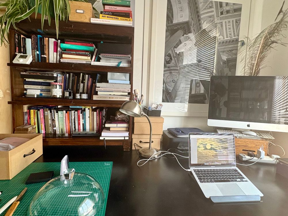 Desk. Which is an old printer’s table liberated from a university. The usual office equipment plus a bookcase and a flattish glass dome. 