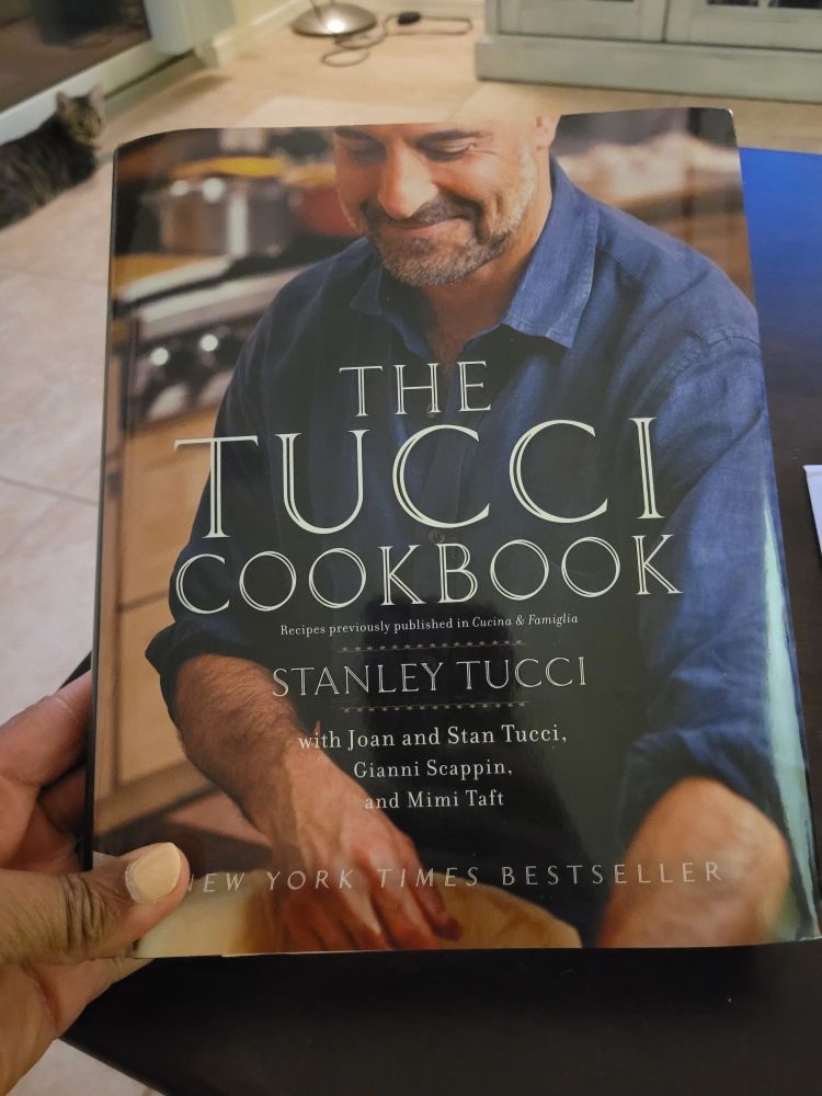 Cover of The Tucci Cookbook by Stanley Tucci hardcover version. My fingers holding in lower left corner.
Bob, a cat lounging in upper left background.