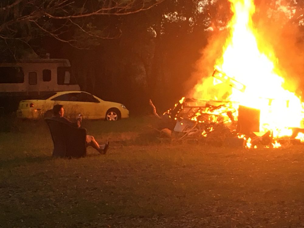 A man (my dad) sits in front of a bonfire that’s at least 12 feet tall and rages dangerously with assorted scrap. 