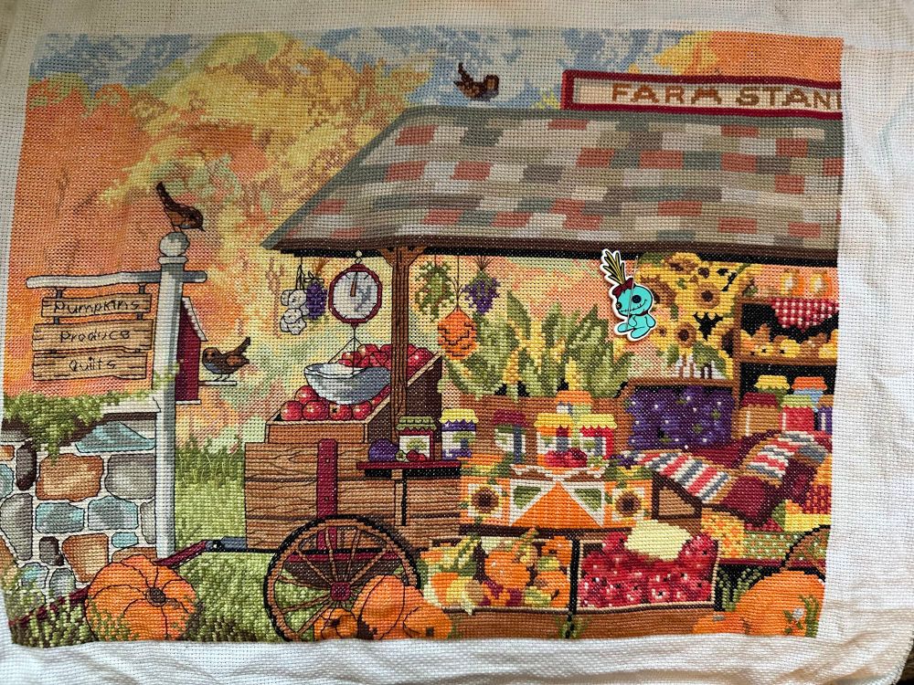 Long story short…it’s a fall scene done in counted cross stitch. Depicts a wooden farm wagon full of corn, apples, gourds, pumpkins on the ground, and quilts, jams and jellies. 
