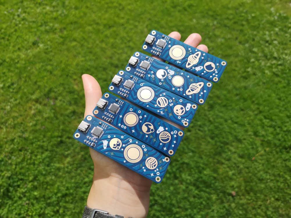 a hand holding 5 PCBs. Each looks a little different but they all show 3 planets and have a usb-c connector