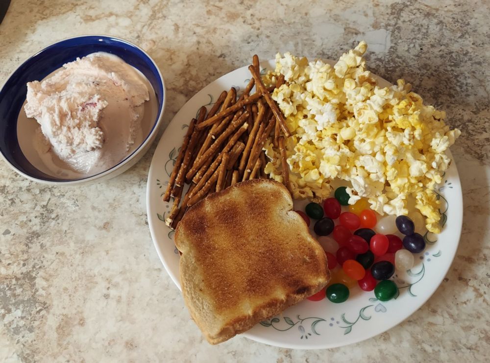 A Charlie Brown Thanksgiving dinner consisting of pretzel sticks, popcorn, buttered toast, jelly beans, and strawberry ice cream. 