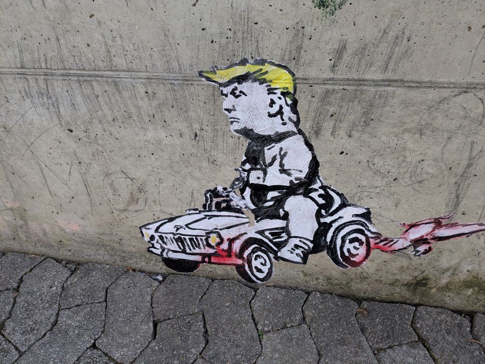 Banksy-style street art showing a baby Trump riding a toy car. 