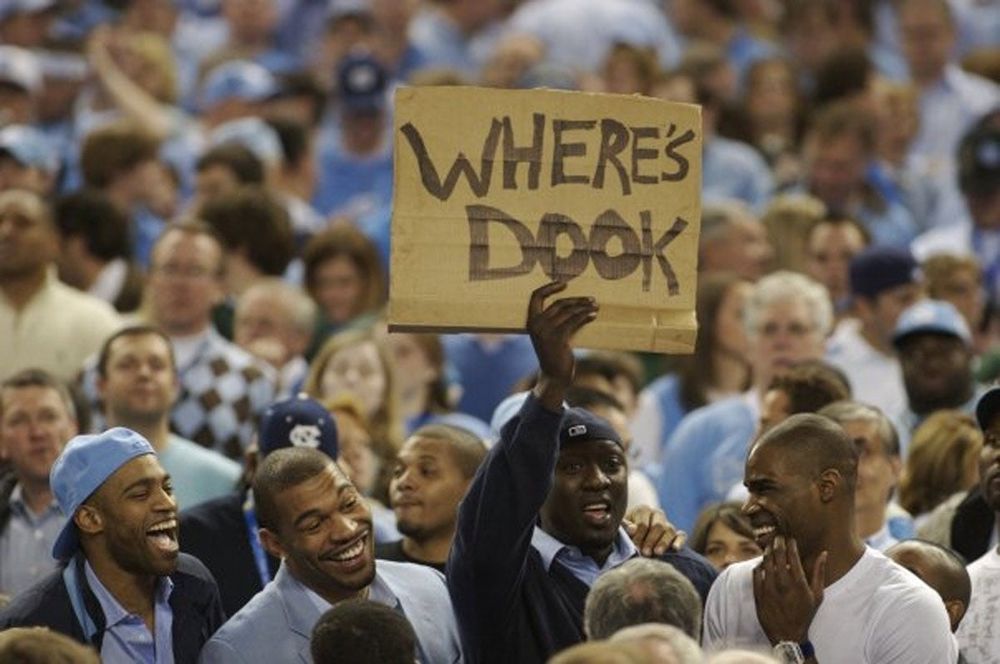 a North Carolina fan holding up a sign that says "where's dook" UNC and Duke are rivals, this was the NCAA men's basketball tournament aka March Madness, they're both usually very good and contenders and in the tournament, but Duke lost early in the tournament that year) 